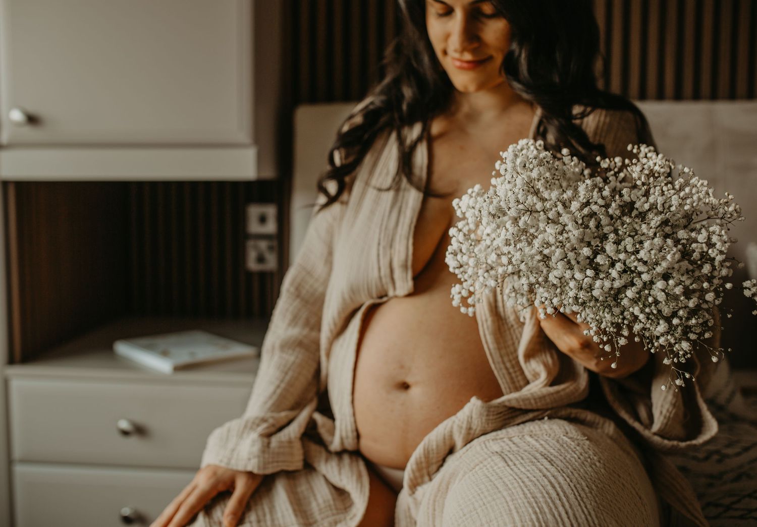 A maternity photo featuring baby's breath flowers and a flowing white dress in warm, moody lighting.