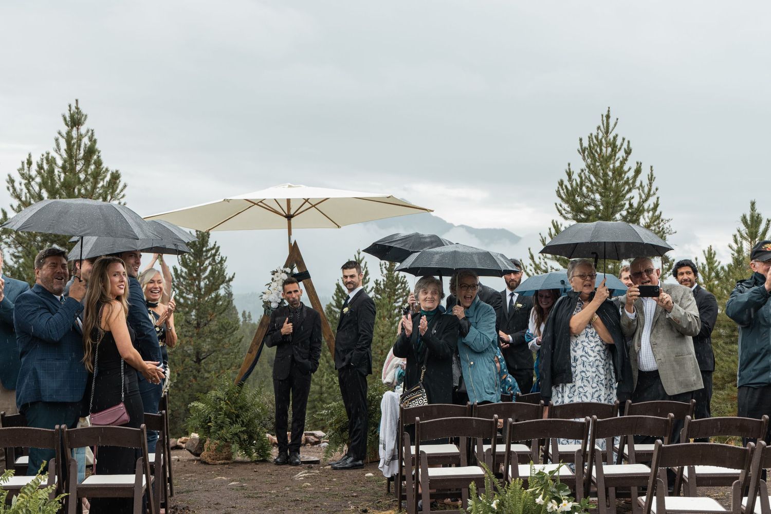 A group gathers under umbrellas on a scenic overlook during an outdoor event with cloudy skies.