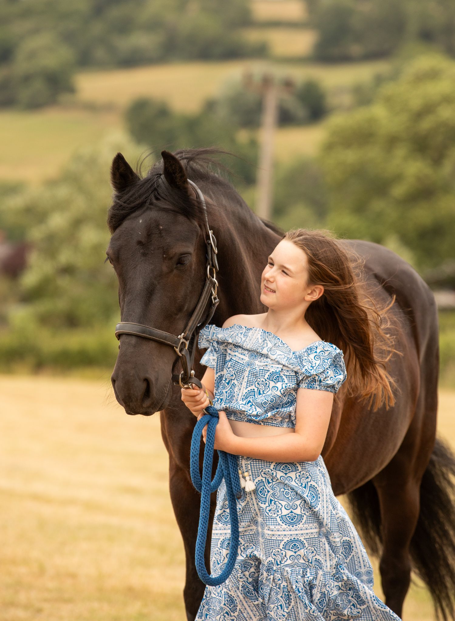 A brown horse and person stand together in a woodland clearing filled with blooming bluebells.
