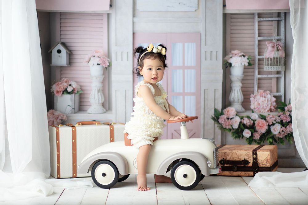 Baby photoshoot with vintage toy car and pink floral backdrop.