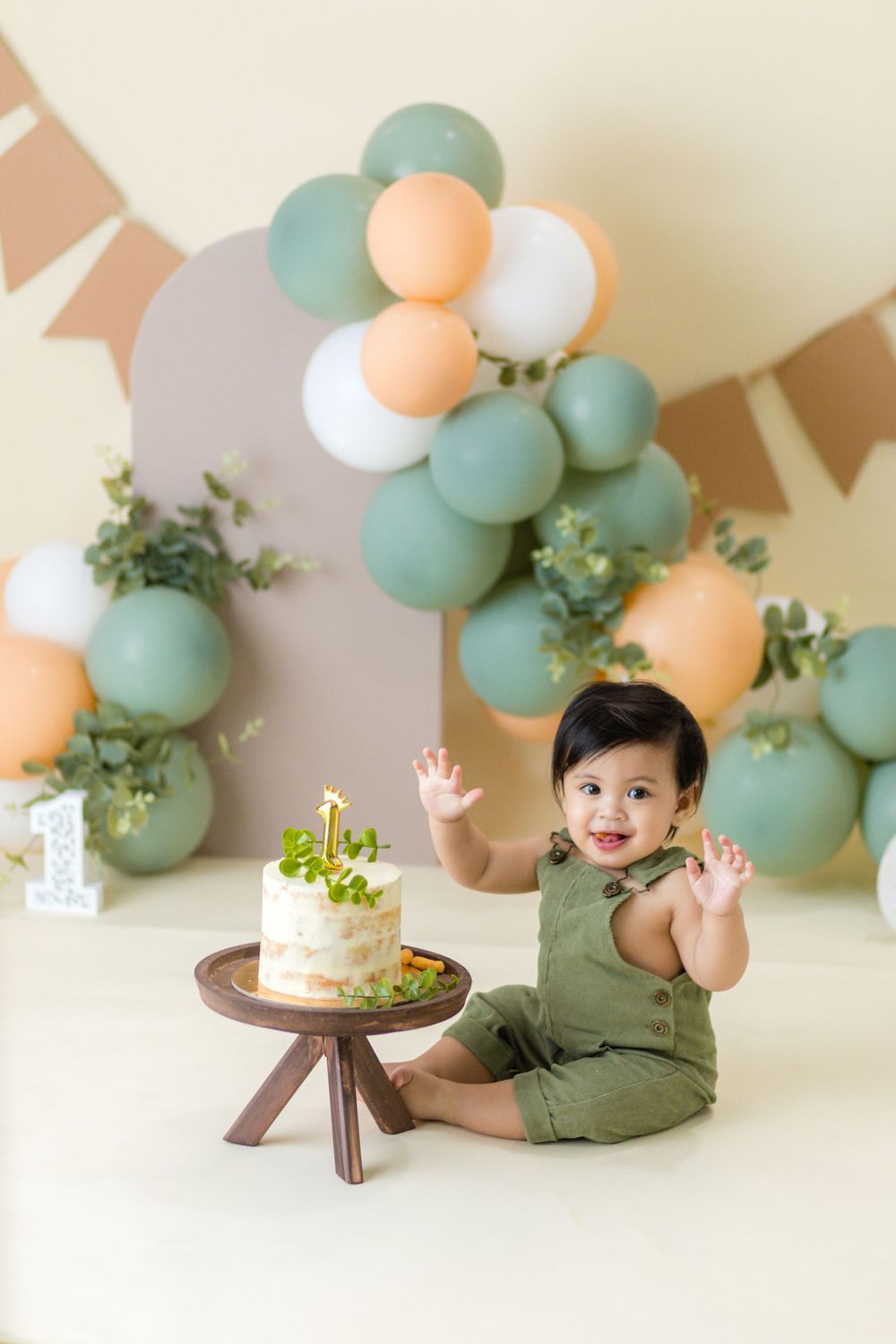 Baby's first birthday scene with mint and peach balloon arch and small white cake.