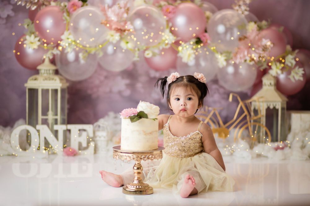 First birthday celebration setup with pink balloons, lanterns and baby with cake.
