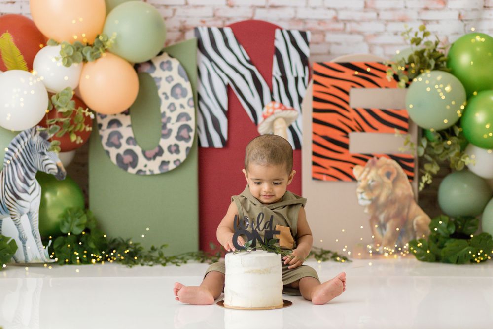 Safari themed birthday setup with jungle animals, green and peach balloons, and smash cake celebration.