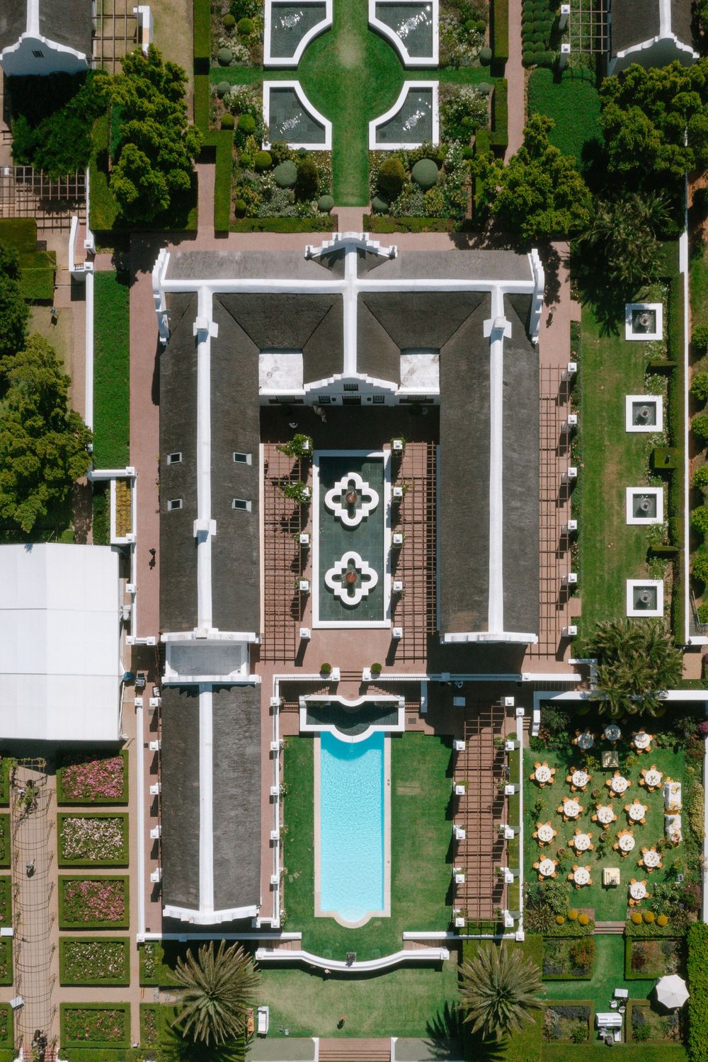 Aerial view of a luxury resort with geometric pools, manicured gardens and symmetrical walkways seen from above.