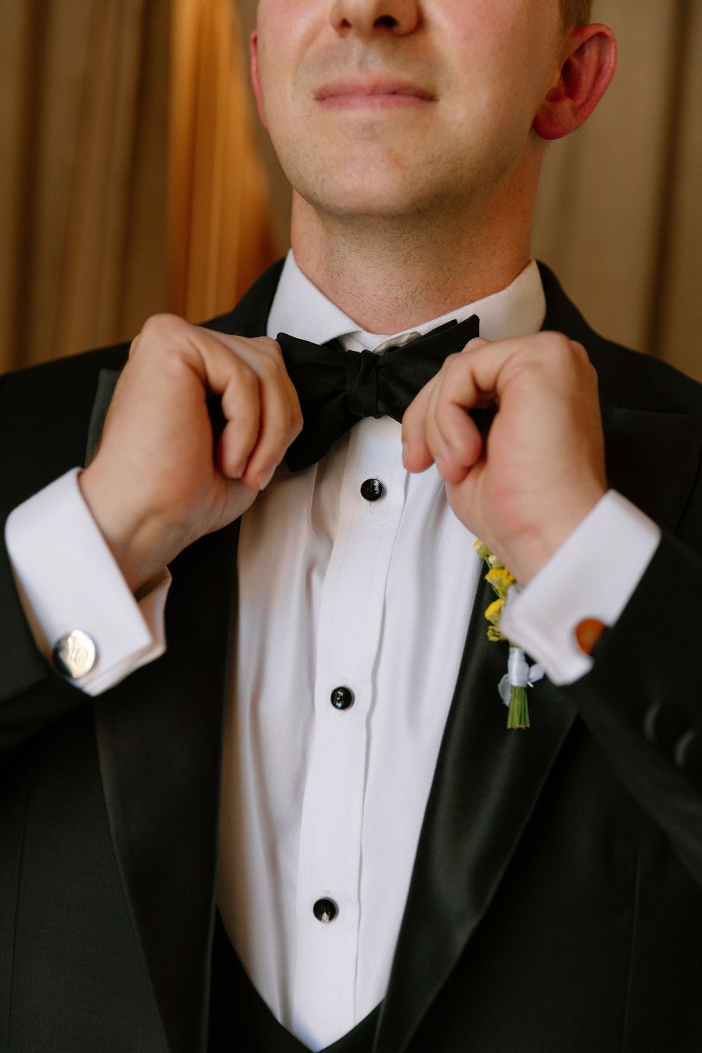 A formal black tuxedo and white dress shirt with a boutonniere being adjusted.