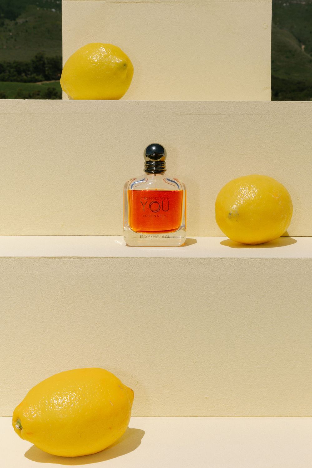 A minimalist still life composition featuring bright yellow lemons and a small perfume bottle on a white surface.