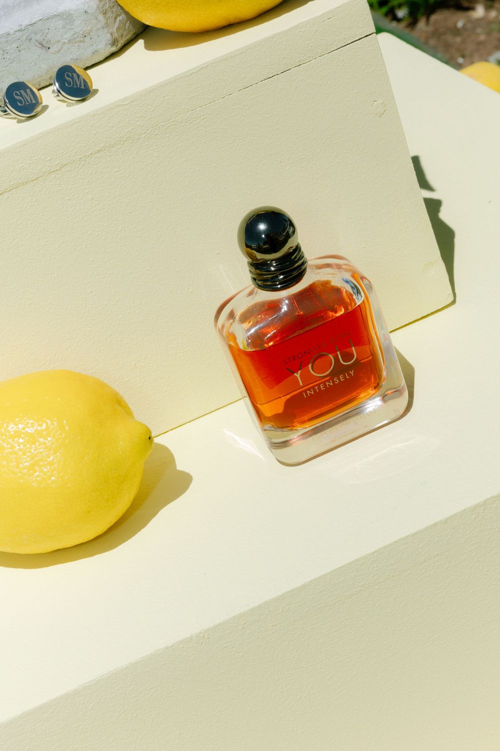 A yellow lemon and small amber perfume bottle arranged on a white surface in bright sunlight.