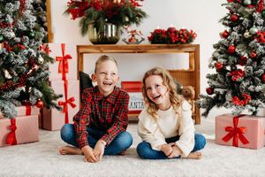 Festive holiday scene with Christmas tree, red decorations and family members lounging on floor by presents.
