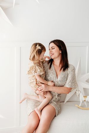 Mother and daughter in matching sequin outfits share joyful moments together on white floor.