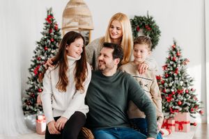 Couple sits together on couch sharing intimate moments in front of decorated Christmas tree with red presents.