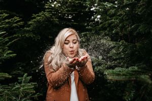 Person in brown leather jacket poses playfully in autumn forest setting.