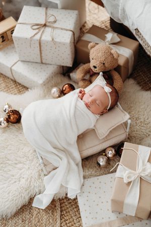 Cozy holiday scene with wrapped presents, teddy bear, and white blanket on neutral textured background.