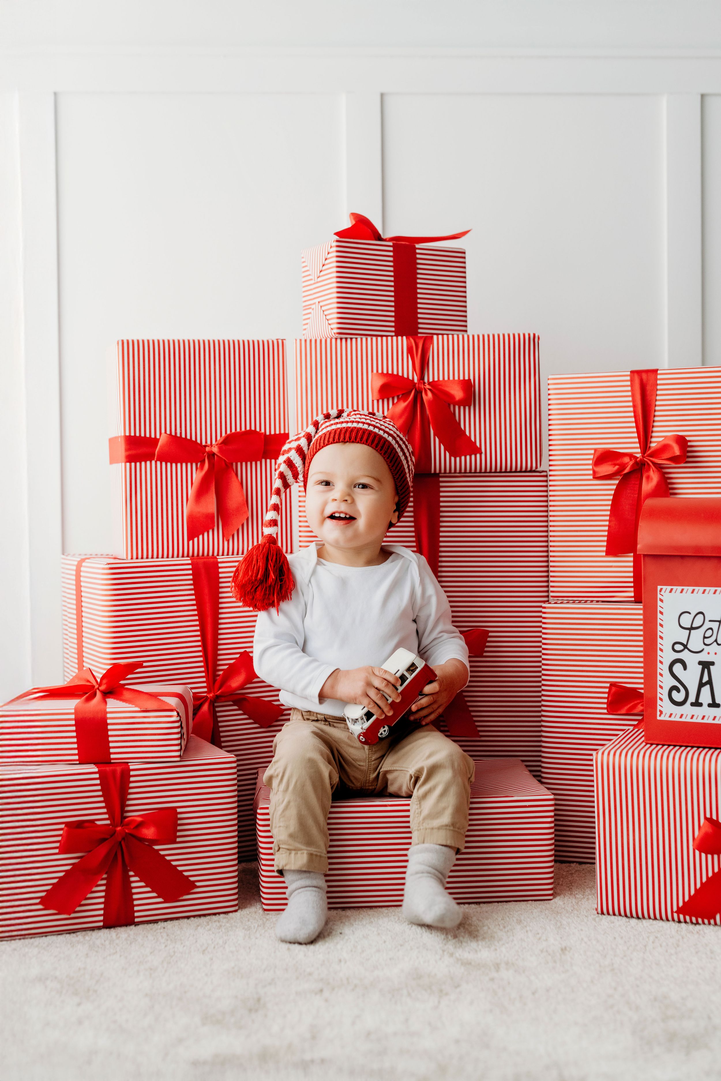 Festive holiday scene with red and white striped gift boxes and bows arranged around a small child in white and khaki.