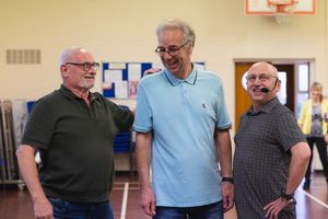 Three men in casual attire share a laugh together while standing in a Letchworth community centre.
