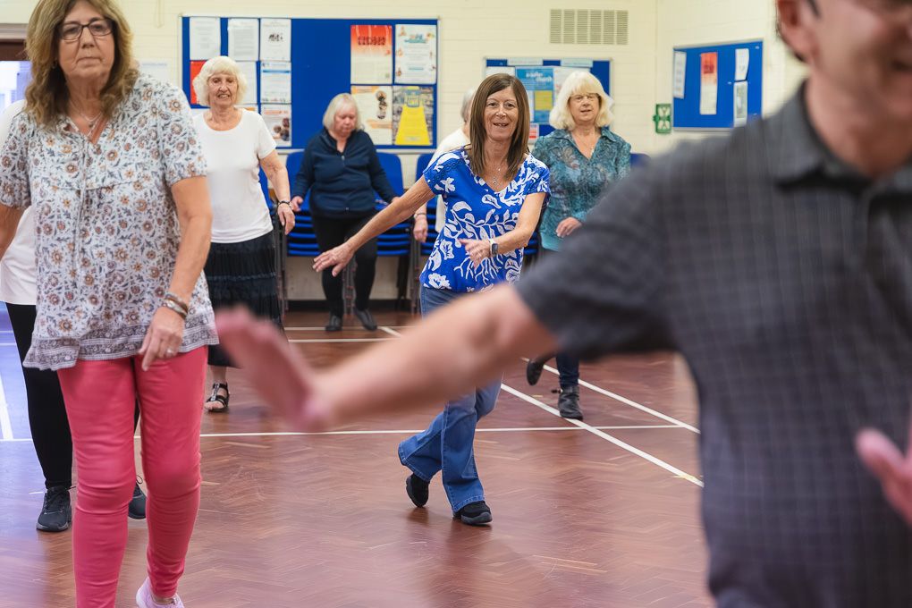 People dancing together in a gymnasium during a social dance class in Hertfordshire.