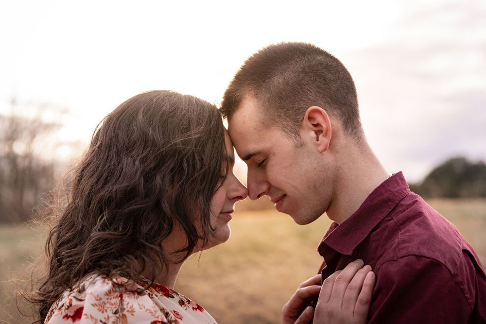 A romantic couple shares an intimate kiss in a field at sunset with a dreamy golden glow.