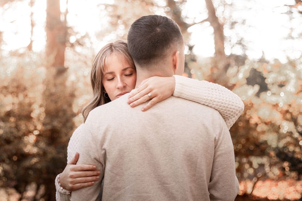 Two people share a tender embrace outdoors during golden hour with autumn foliage in the background.