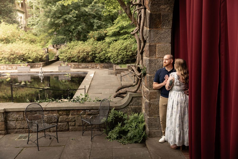 A rustic outdoor wedding venue features stone walls, red curtains, and elegant garden seating arrangements.