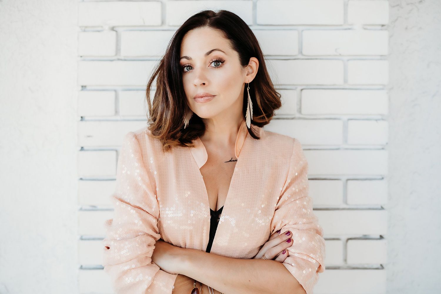 Professional wearing a peach-colored blazer poses against a white brick wall in a modern studio setting.