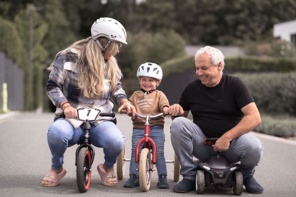 Eine Familie bringt einem kleinen Kind in einer Wohnstraße das Laufradfahren bei.