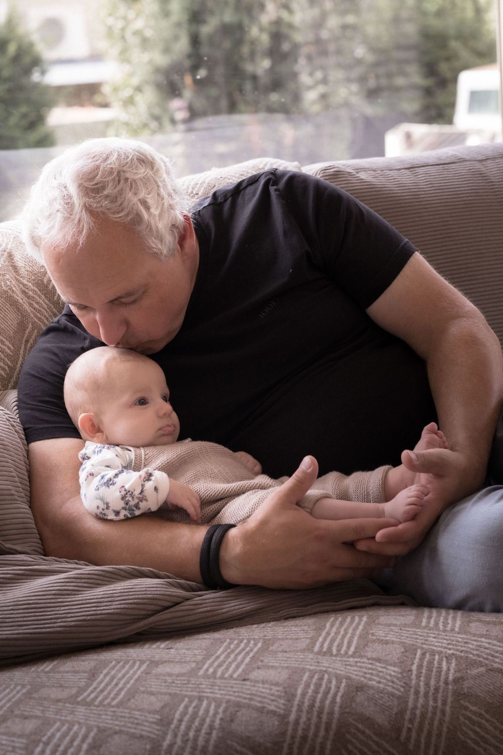 Erwachsener und Baby liegen zusammen auf einem braunen Cordsofa und zeigen eine Abfolge entspannender Positionen.