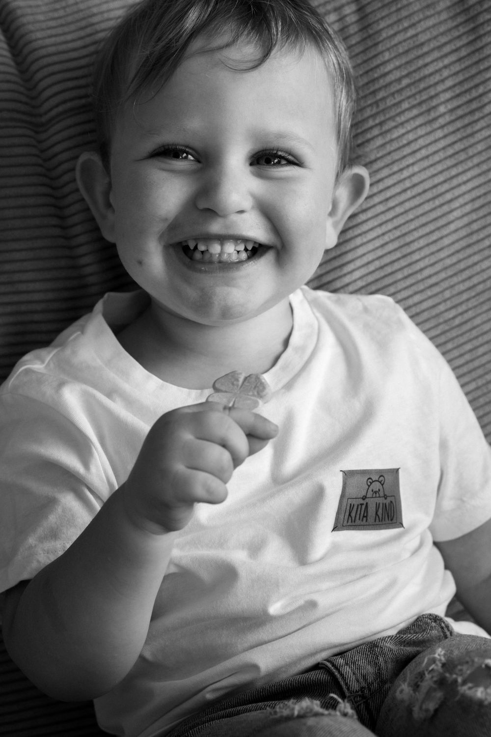 Schwarz-Weiß-Porträts eines lächelnden Kleinkindes im weißen T-Shirt auf der Couch.