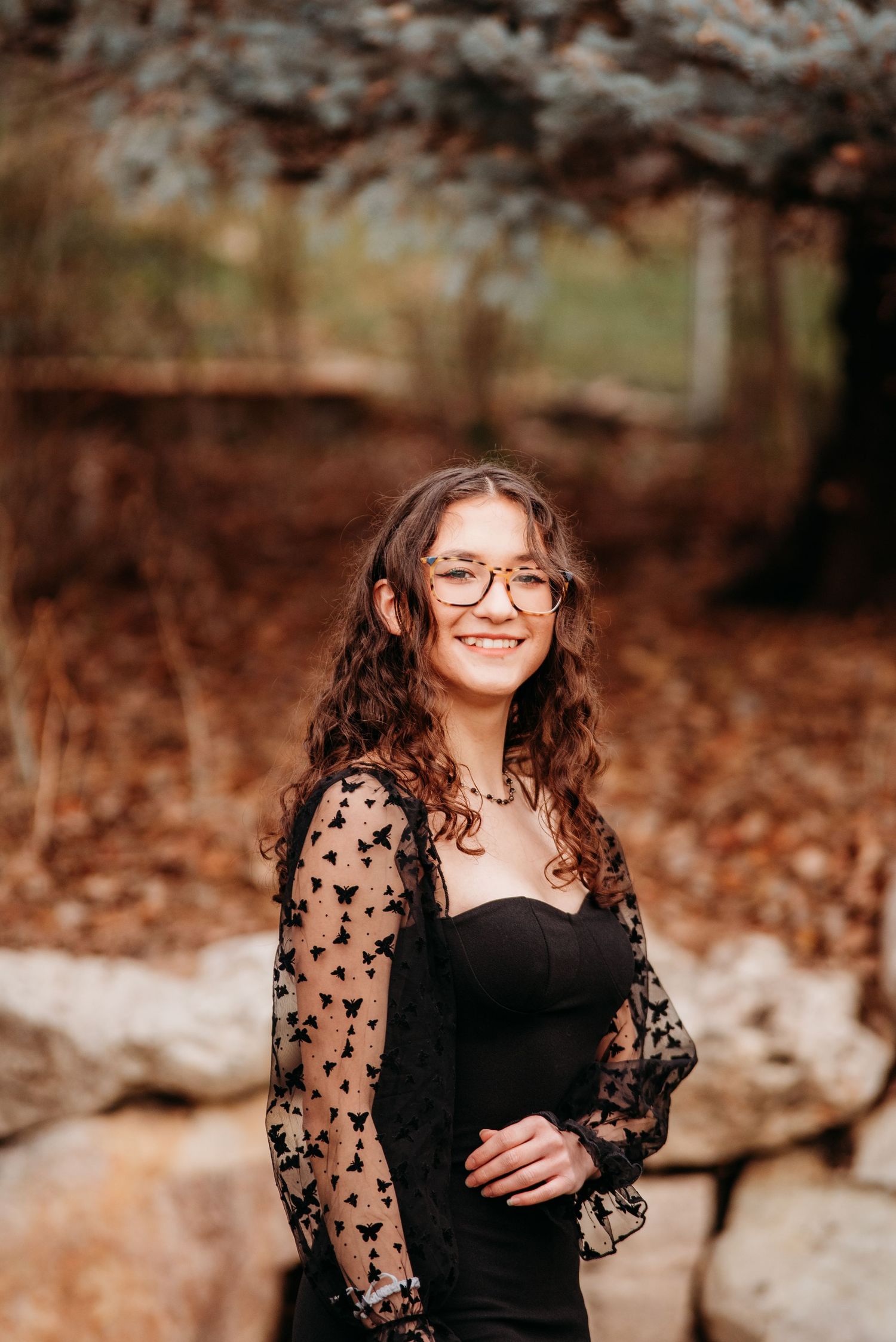 Woman in black dress with sheer star-patterned sleeves smiling outdoors in autumn setting.