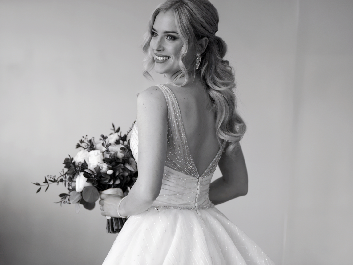 Black and white portrait of a bride in an elegant backless wedding gown holding a floral bouquet.