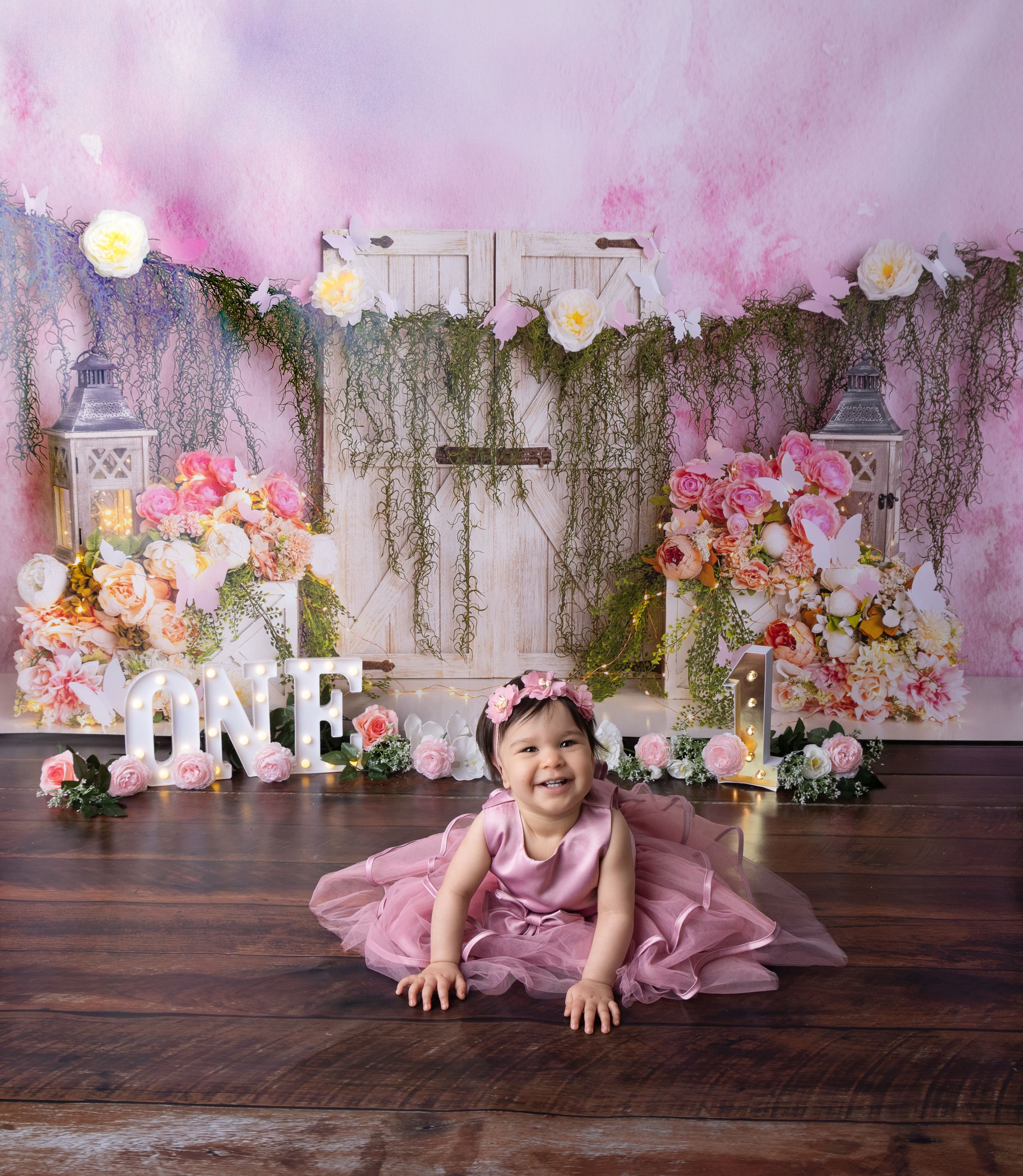 Dreamy first birthday photoshoot scene with pink dress and floral decorations.