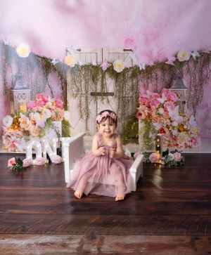 First birthday photo session with pink florals and white ONE letters against rustic backdrop.