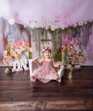 Pink floral first birthday setup with white letters and rustic decorative elements.