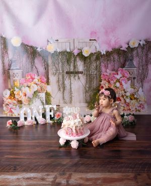 Vintage-style birthday scene with pink florals, hanging moss, and white 'ONE' letters against rustic backdrop.