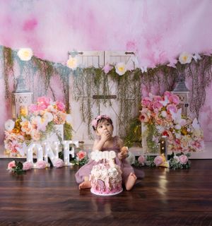 Pink floral birthday Cakesmash setup with white lettering, moss accents, and vintage door backdrop.