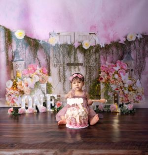 Elegant first birthday photo setup with floral arrangements and rustic backdrop with string lights.