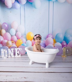 White bathtub setup with pastel balloon backdrop and 'ONE' letters for first birthday photo shoot.