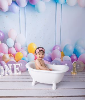 Colorful balloon backdrop with white antique bathtub and 'ONE' letters for first birthday session.