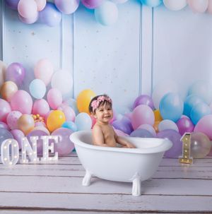 First birthday photo setup with white clawfoot tub and pastel balloon wall decoration.