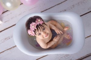 Milk bath photo setup with pink floral accents in white vintage-style tub.