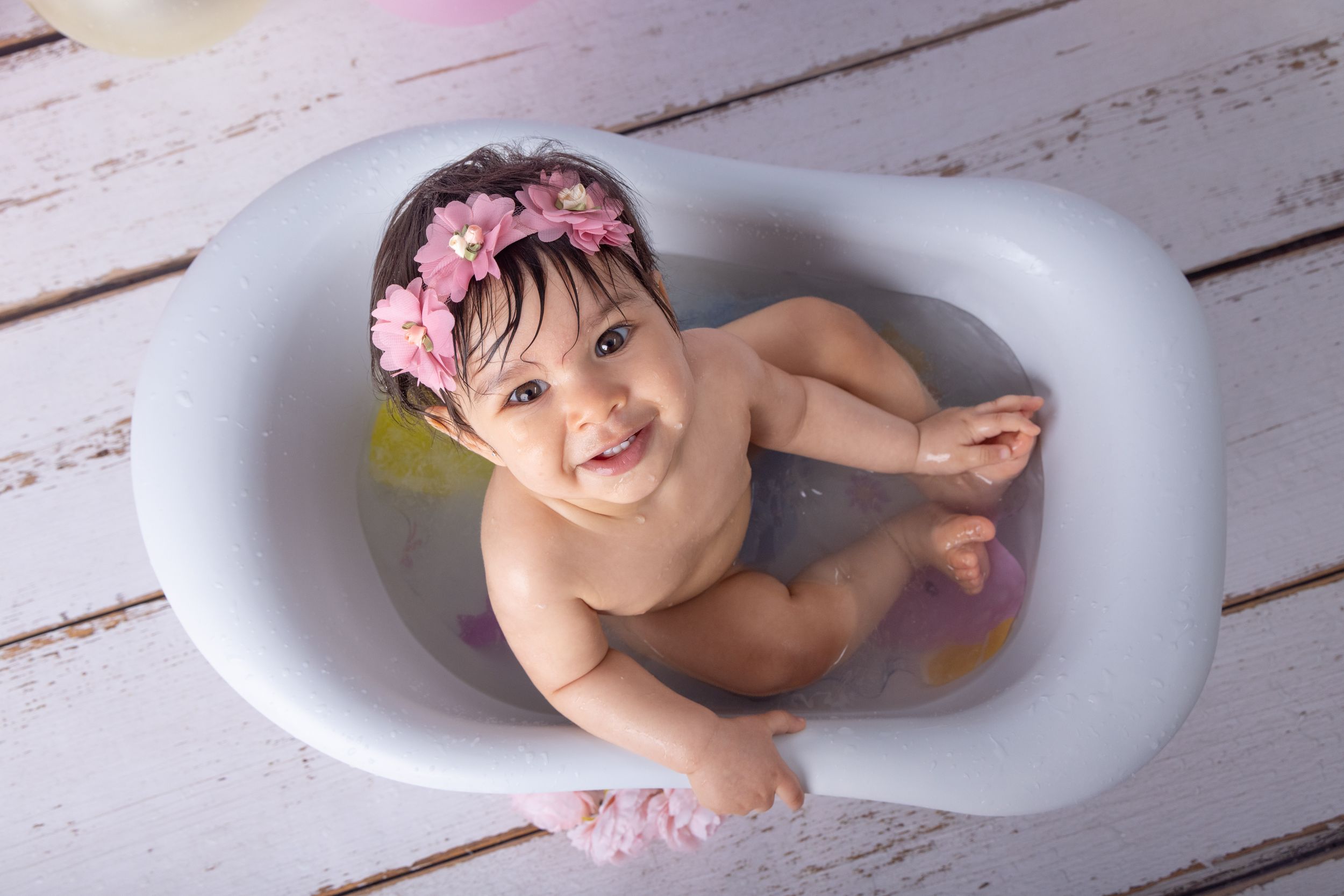 Baby bathing photo session features fun moments in a white bathtub with bubbles and splashes.