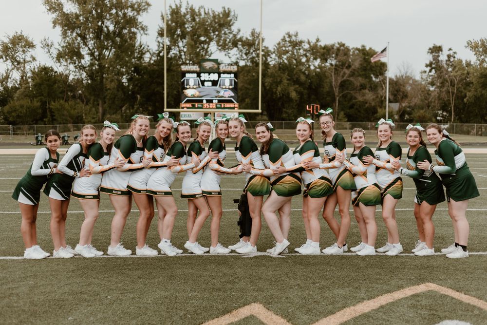 A large high school cheerleading squad in green and white uniforms poses together on a football field.