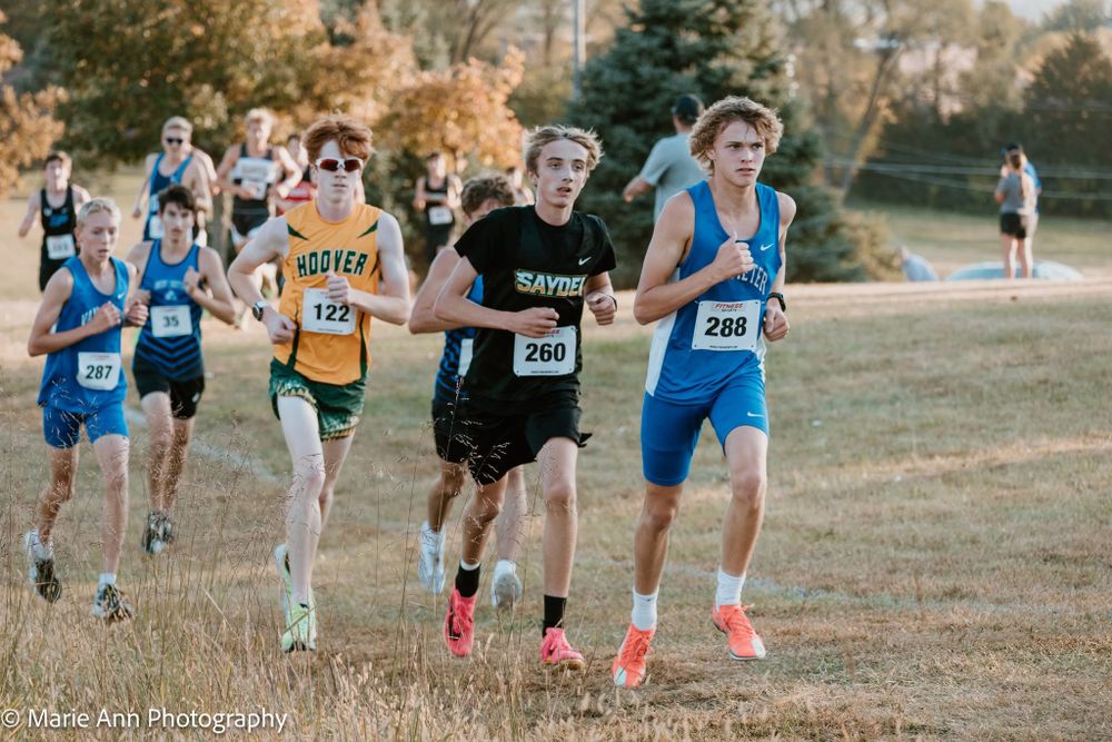 Male cross country runners competing in an outdoor race on a grass field.
