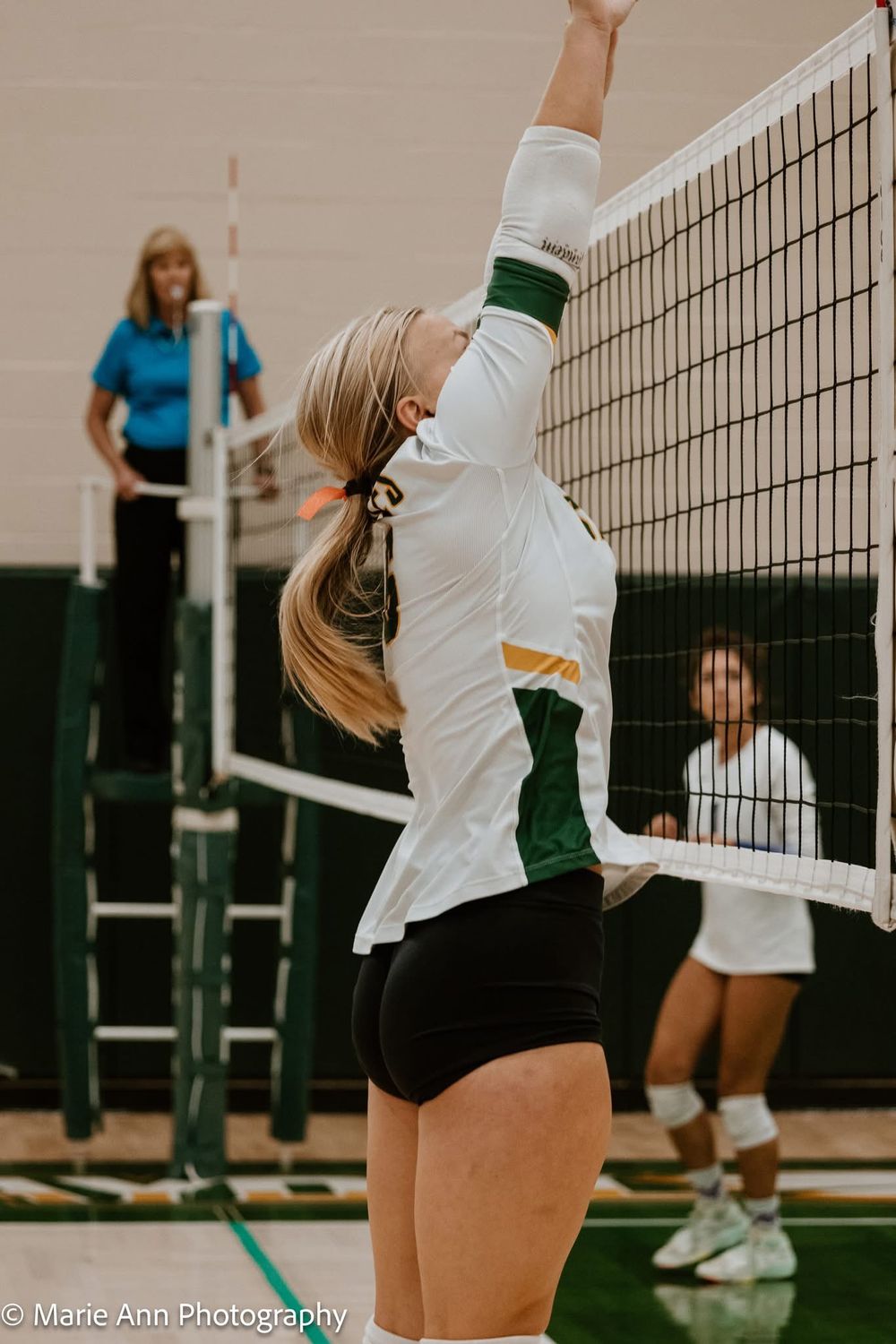 Female volleyball player jumping to spike the ball over the net during an indoor game.