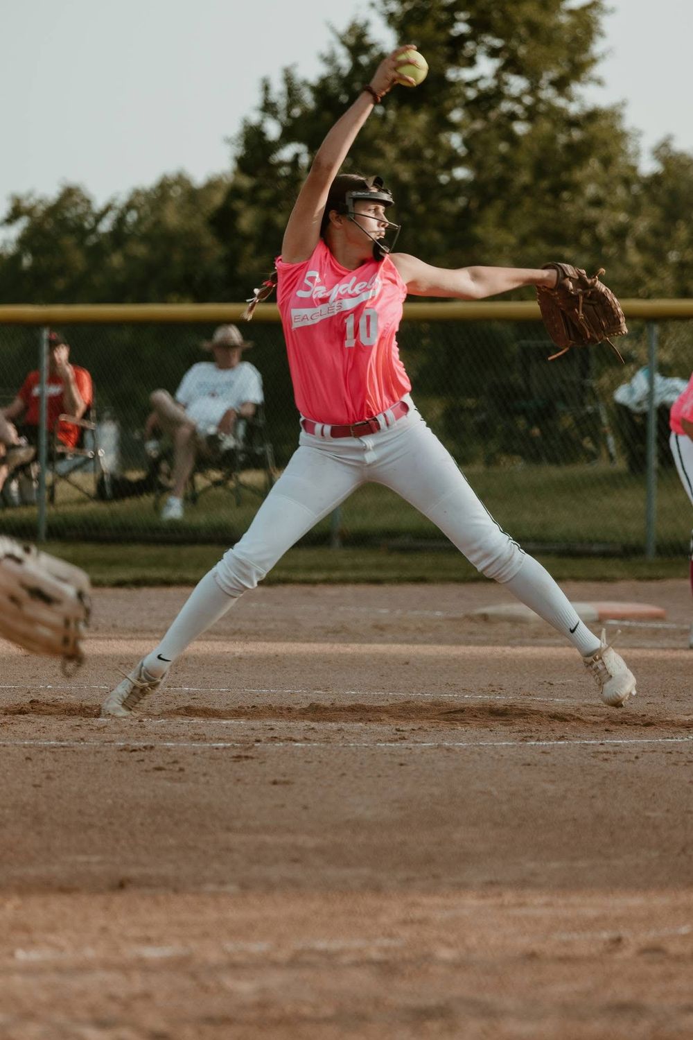Softball pitcher in pink jersey winding up to throw during an evening game.