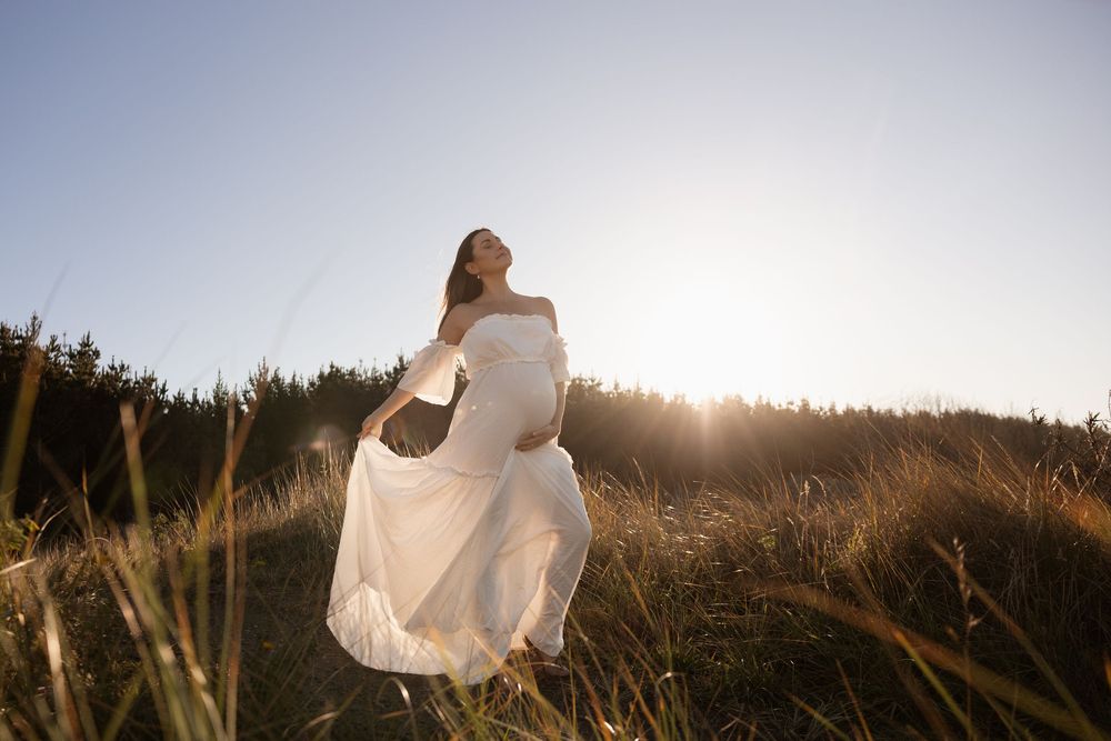 Mum holding her dress out at sunset maternity session at the beach