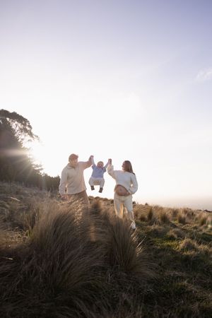 Couple lifting their toddler in the air while mum holding onto bump during sunset maternity/ family session at Port Hills