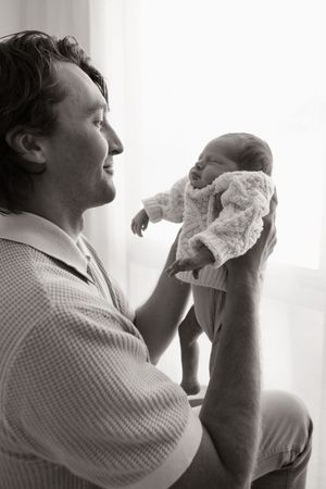 Dad holding newborn baby up and looking at her little scrumch during studio session in Bishopdale