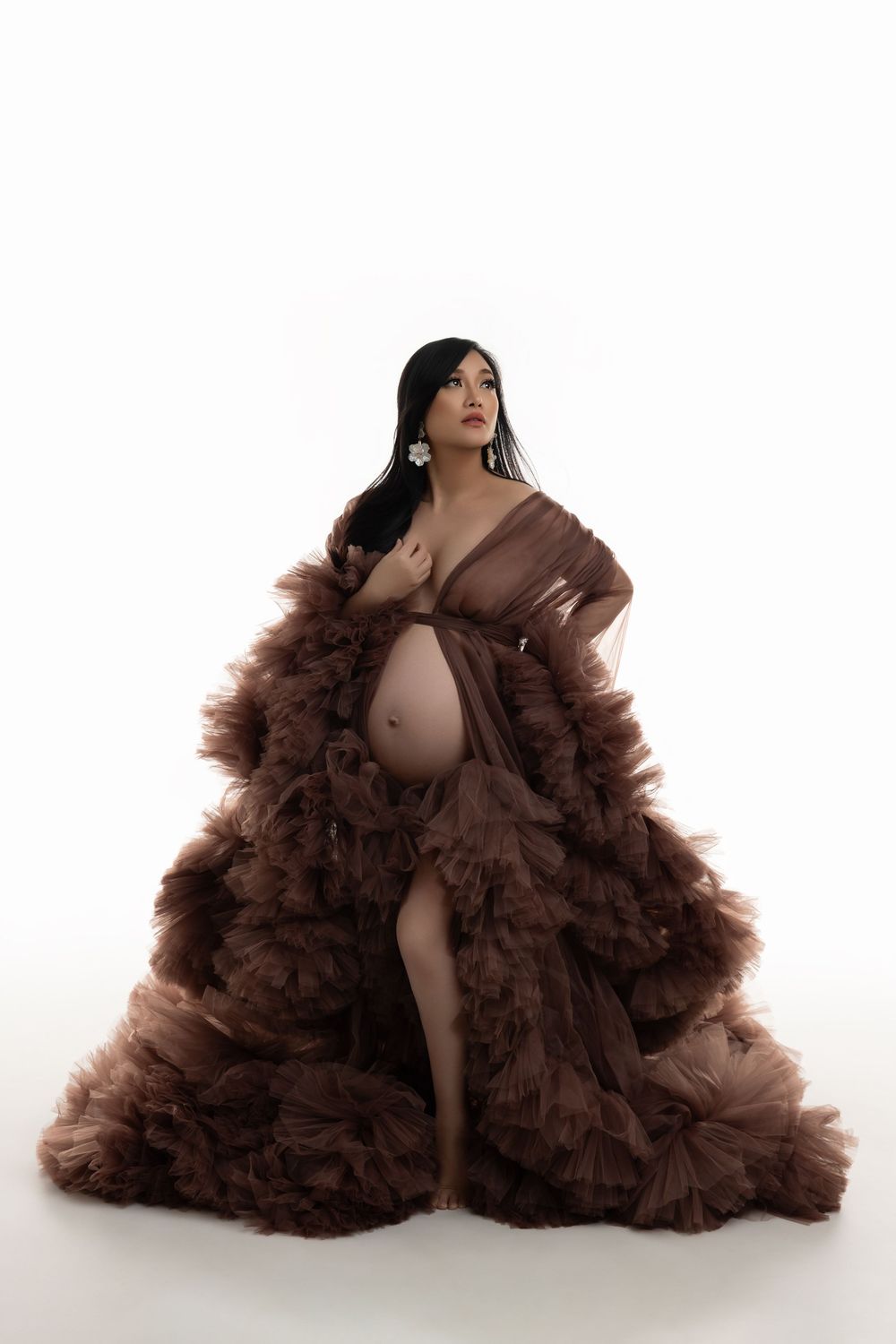 Maternity portrait featuring an elegant brown tulle gown against a white background in a dramatic fashion pose.