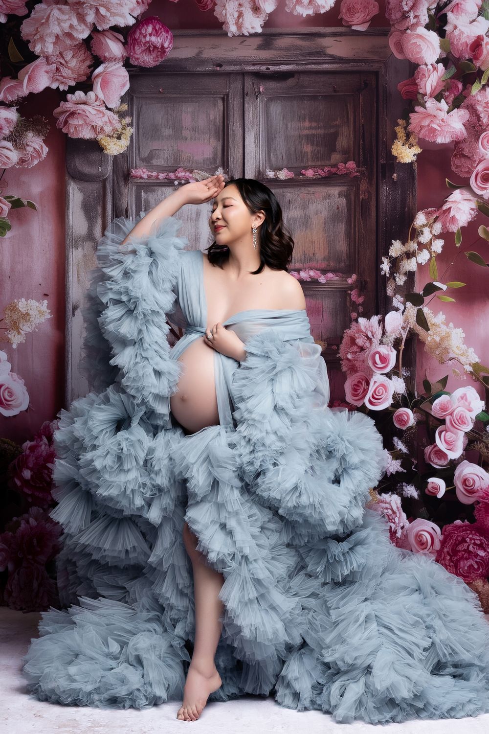 A flowing dusty blue tulle gown creates a dreamy atmosphere against a backdrop of pink cherry blossoms and vintage doors.
