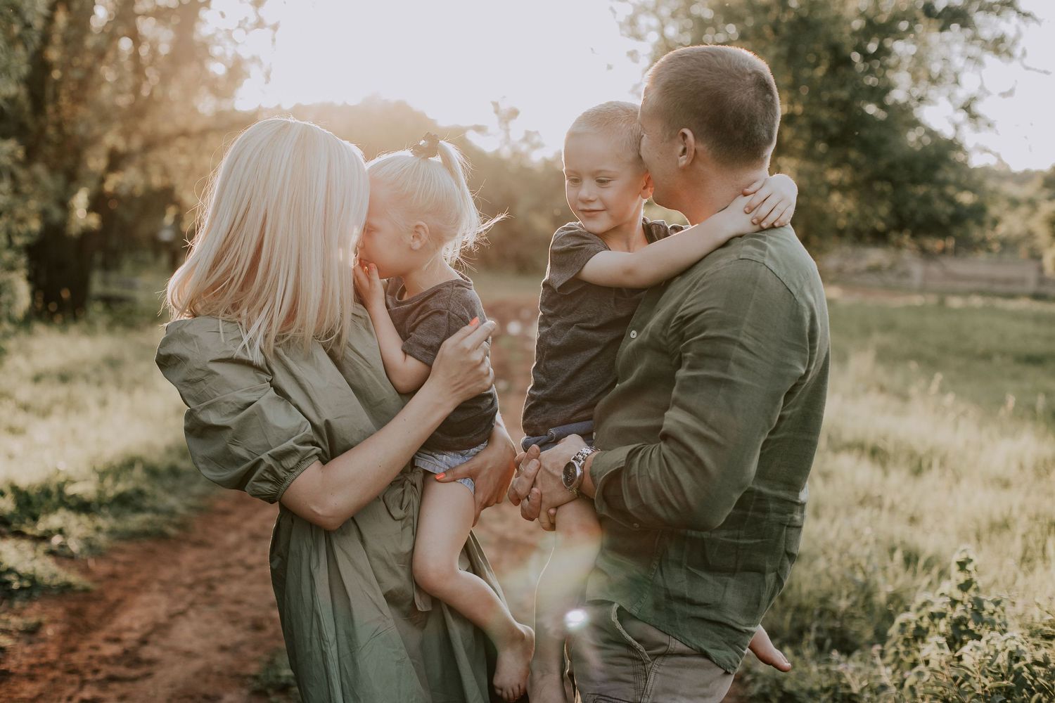 A candid family moment captured in warm sunlight on a dirt path surrounded by natural scenery.