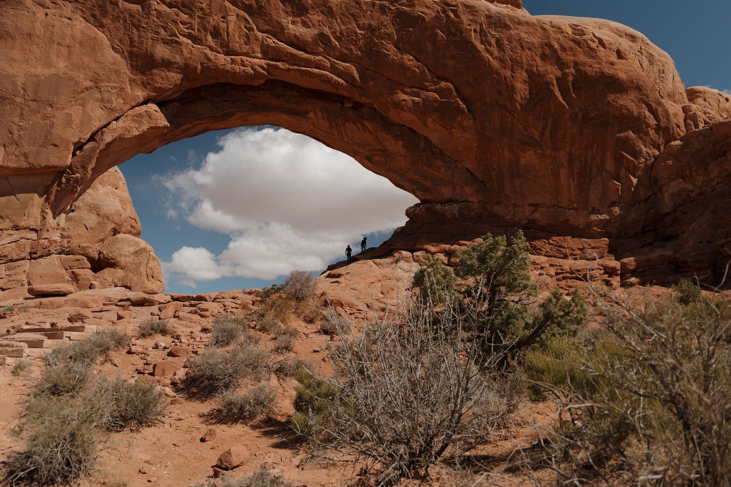Natural stone arch formation spans across desert landscape under blue sky.
